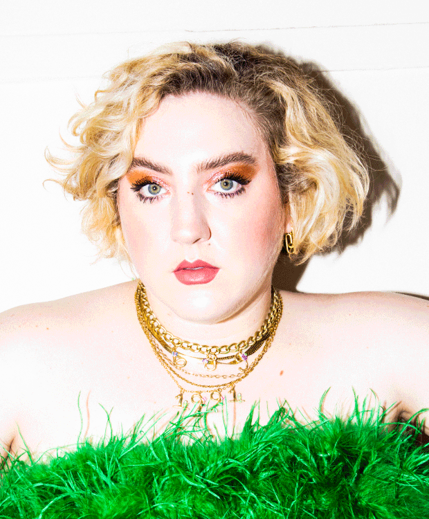 Portrait of a blonde woman wearing gold necklaces and a green feather top